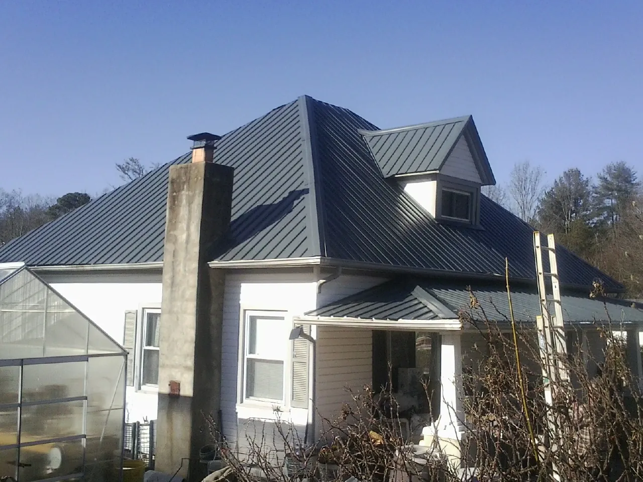 Dark blue standing seam metal roof on a white farmhouse with dormer — Slate & Tile Roof Repair by Roofing Brothers in Stevensburg