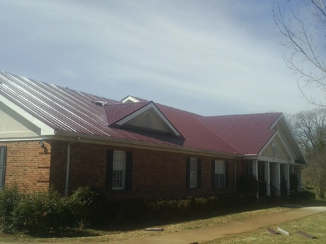 Red metal roof with gabled entries on a long brick building, from a Hail Damage Roof Repair job in Stevensburg