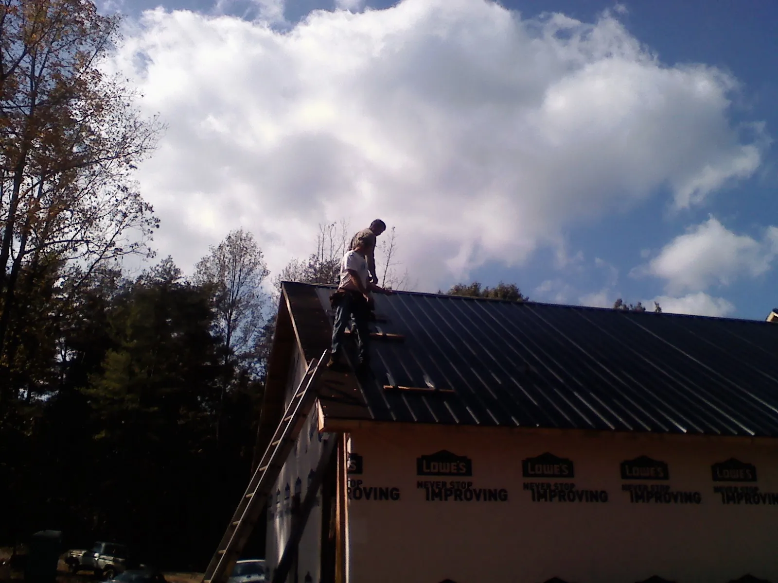 Roofer fastening dark metal panels high against a cloudy sky, from a Roof Inspection job in Stevensburg